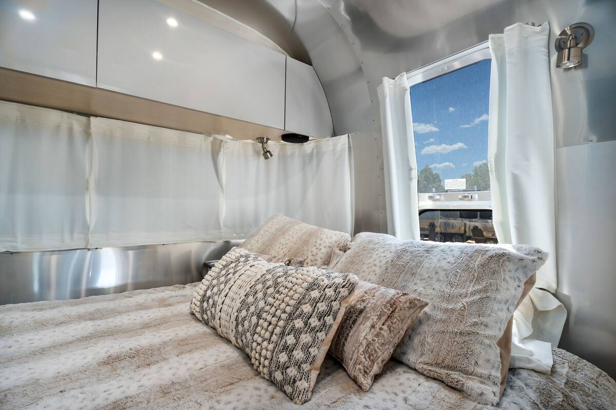A cozy bed with patterned pillows and a view of a train through a window.
