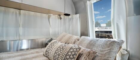 A cozy bed with patterned pillows and a view of a train through a window.
