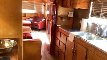 A compact RV kitchen with wooden cabinets, a refrigerator, a sink, and a dining area with a red couch.