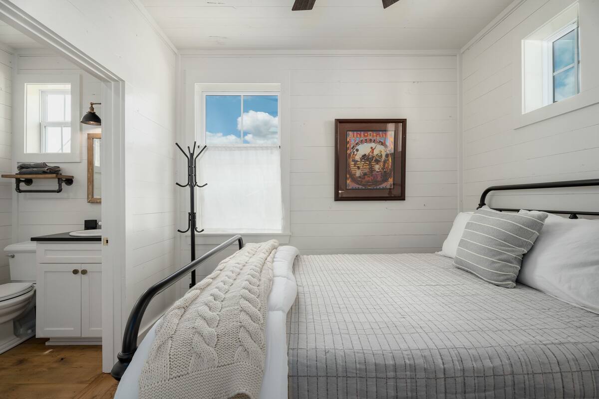 A bedroom with a bed, a window, a framed picture, and a coat rack.