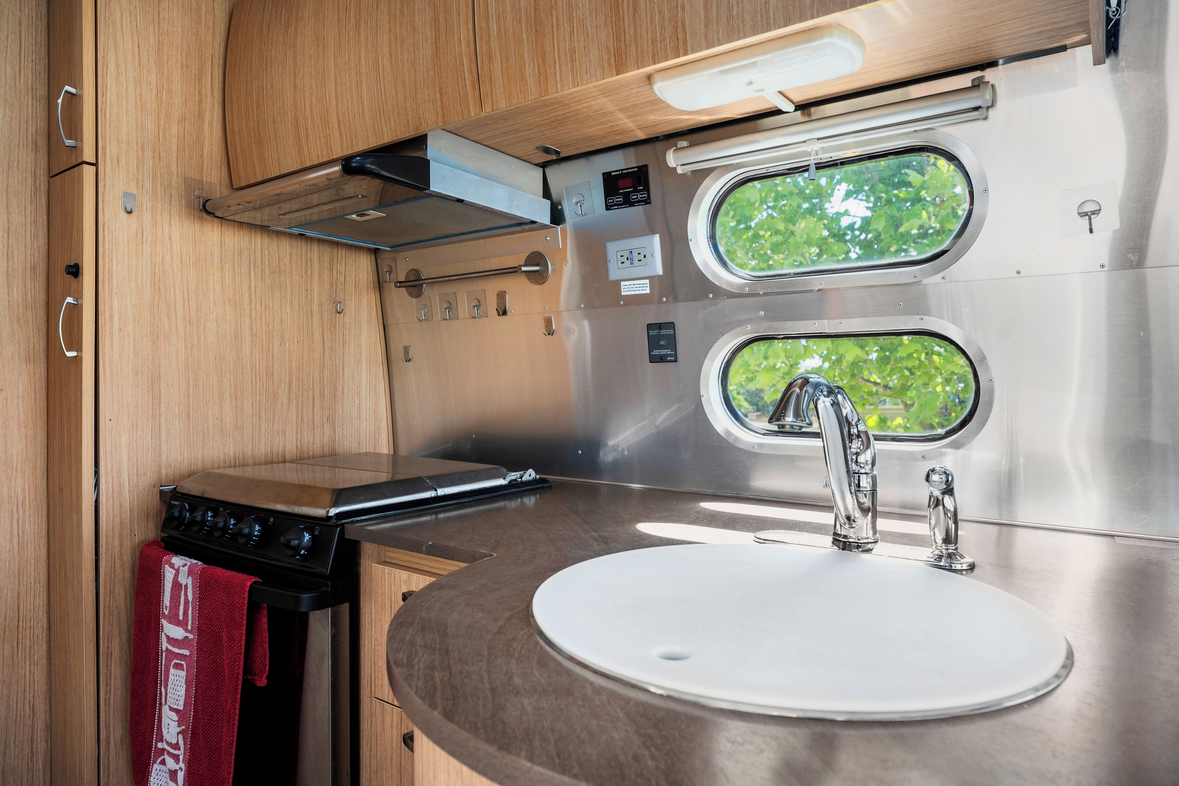 Een compacte kitchenette met een roestvrijstalen spoelbak, een fornuis en twee ramen met uitzicht op groen.