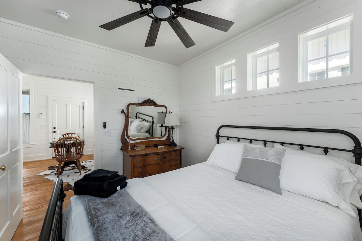 A bedroom with a bed, a dresser, a mirror, and a ceiling fan.