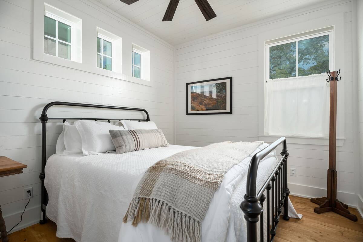 A bedroom with a bed, a bedside table, a window with a view, and a framed picture on the wall.