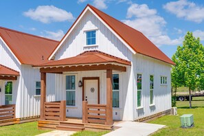 A white building with a red roof, a wooden porch, and a small front door.