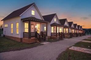 A row of white cabins with wooden decks and a gravel path leading to them.