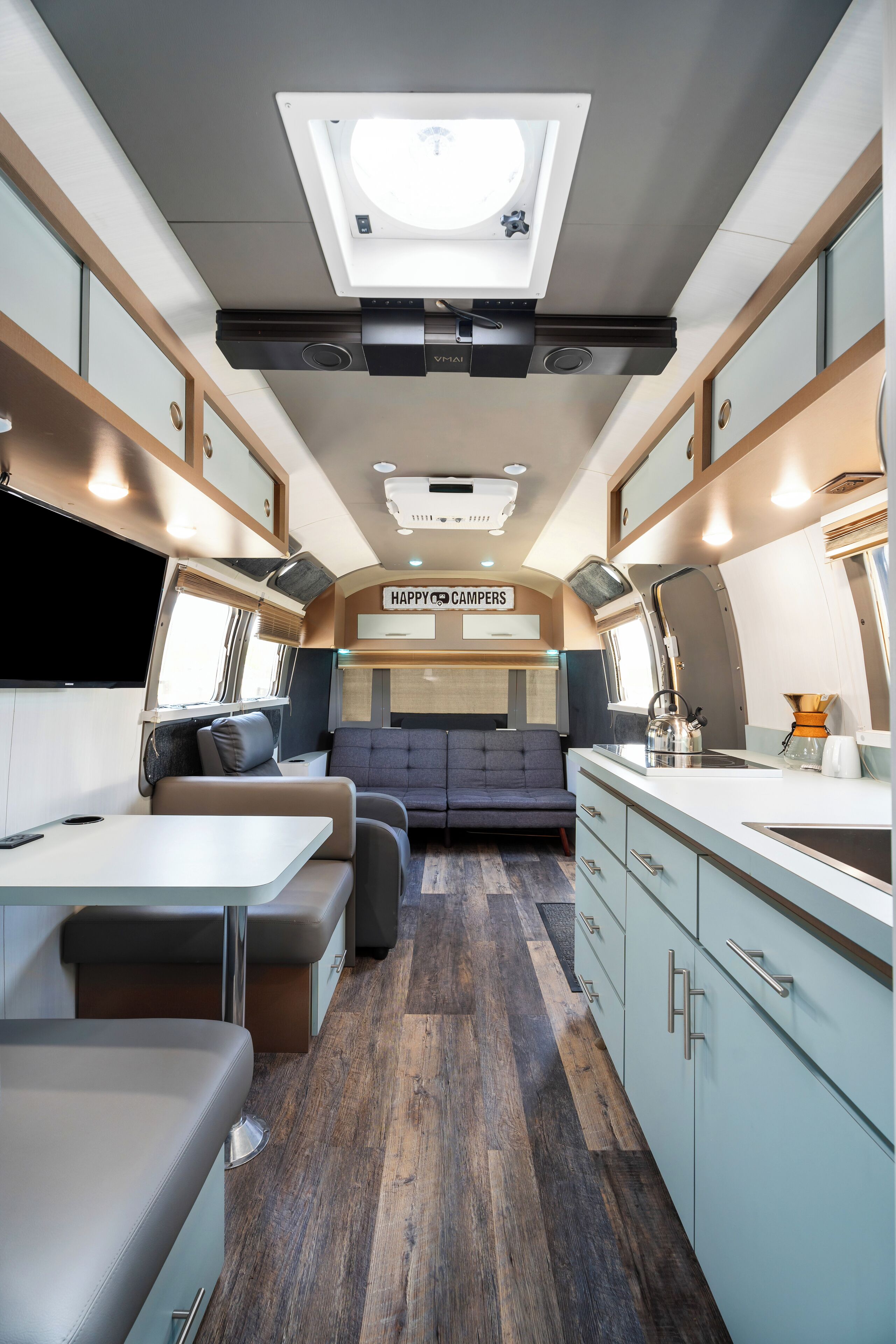 En kompakt autocamper indretning med tekøkken, siddegruppe og en projektor monteret i loftet.