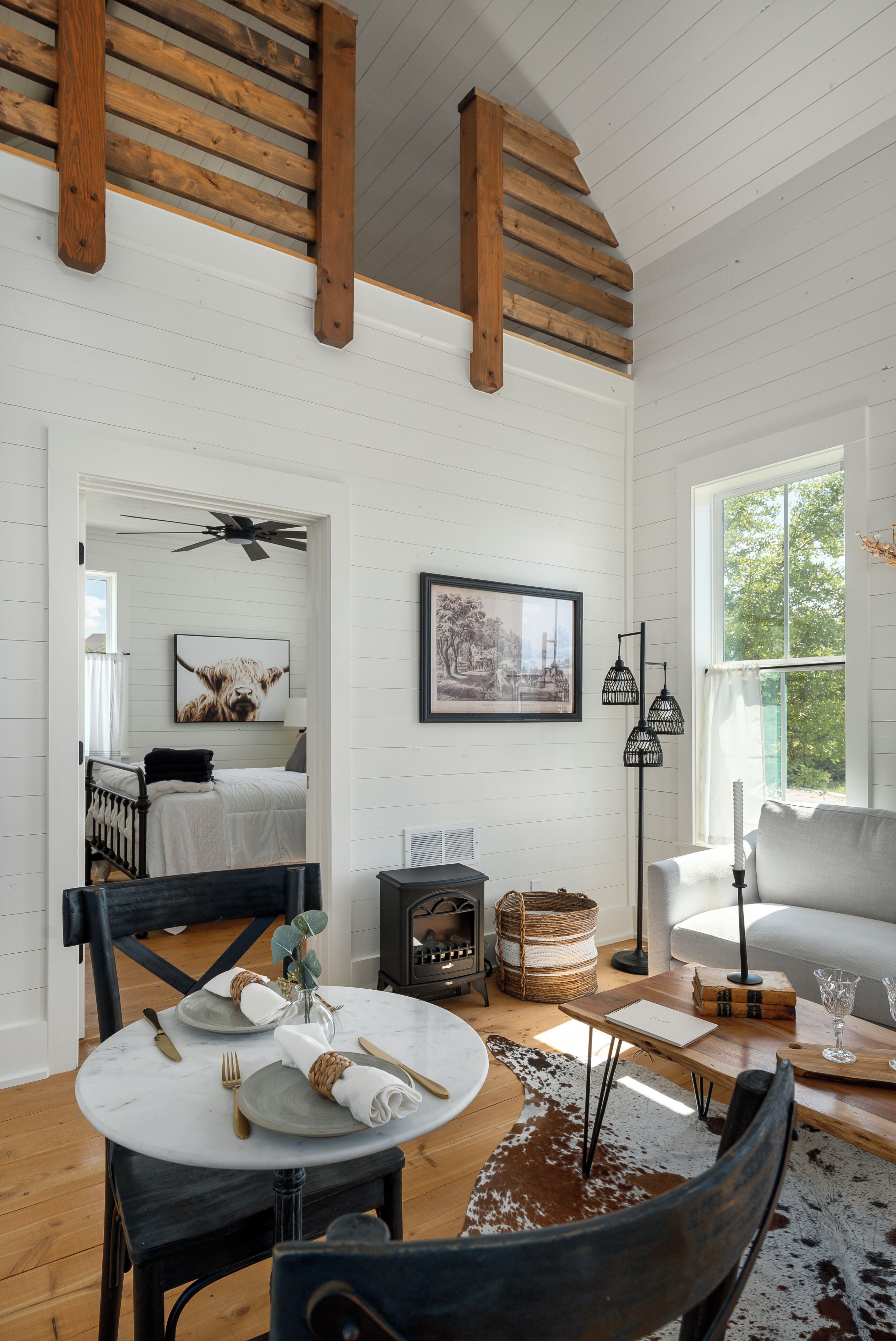 A cozy room with a bed, a dining table set for two, and a large window with a view of greenery.