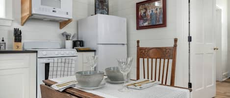 A kitchen with white cabinets, a wooden chair, a table with a white tablecloth, and a refrigerator.