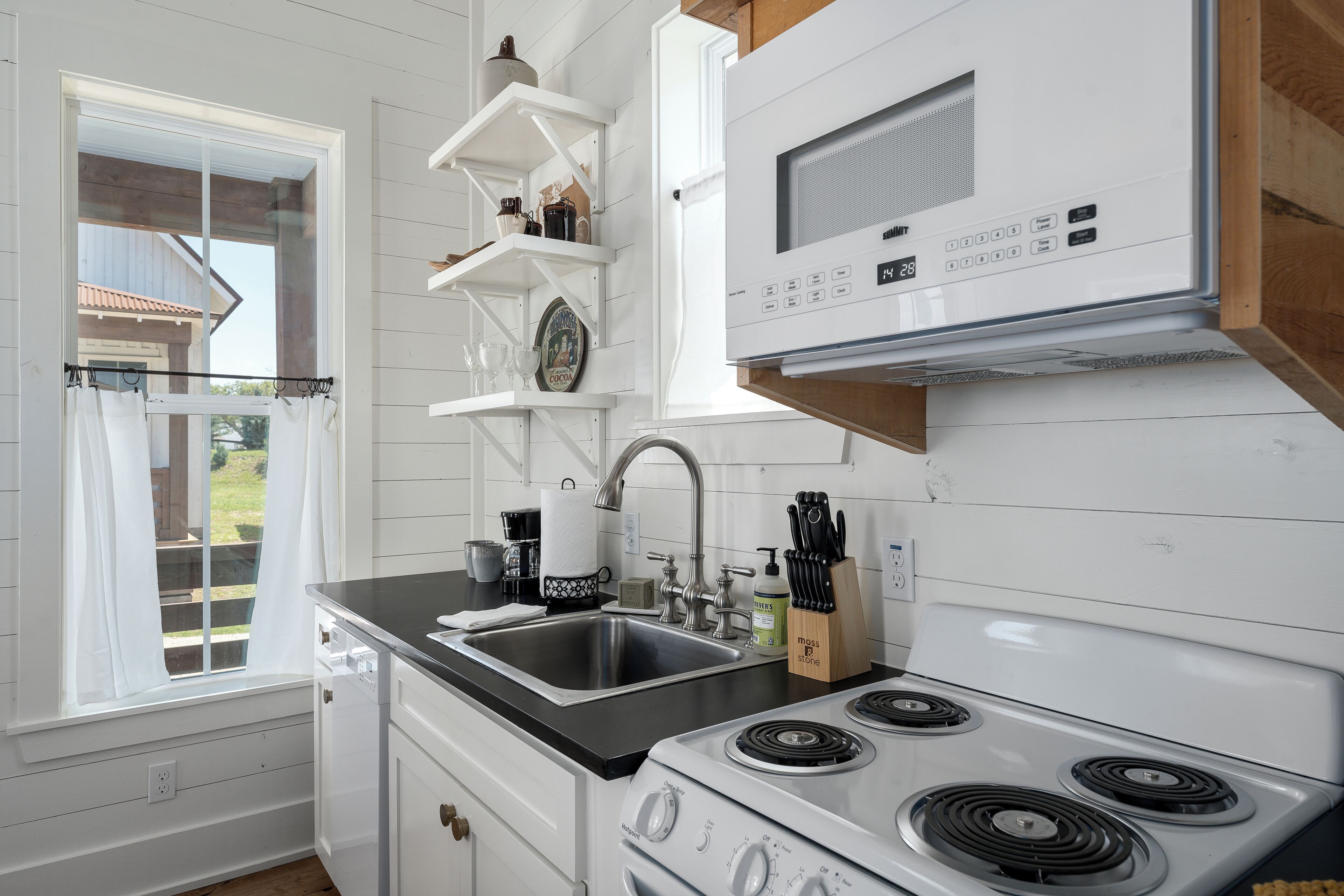 A kitchen with white cabinetry, a black countertop, a stove, and a sink.