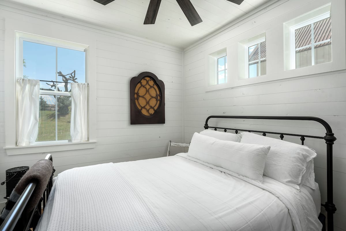 A bedroom with a large bed, white walls, and a wooden ceiling.