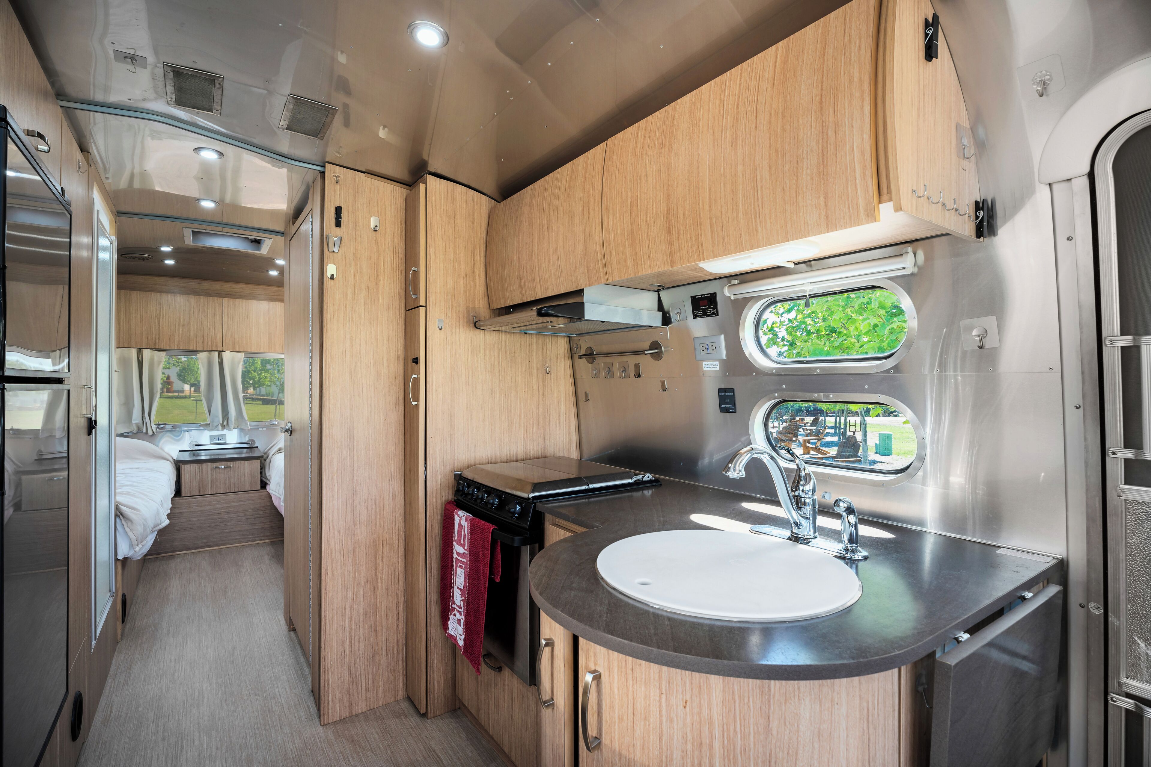 A compact RV kitchen with a sink, stove, and a window providing a view of greenery.
