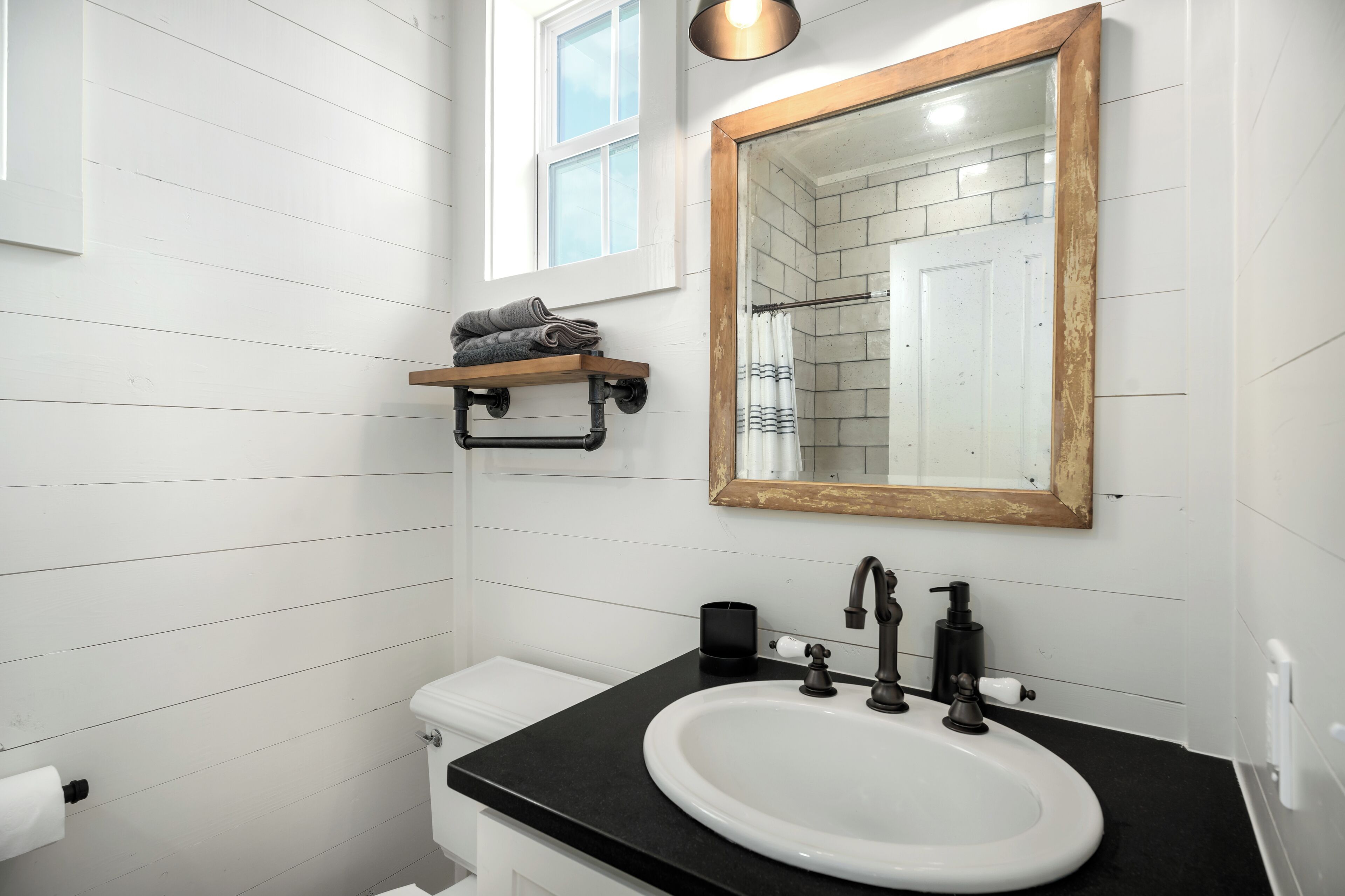A bathroom with a white sink, black countertop, and a mirror with a wooden frame.