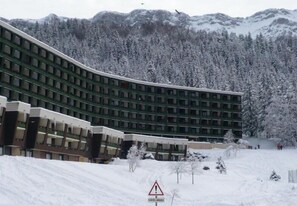 Un edificio de varios pisos con fachada curva, rodeado de árboles y montañas cubiertas de nieve.