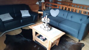 A cozy living room with a black leather sofa, a blue sofa with a heart-shaped cushion, and a wooden coffee table with decorative items.
