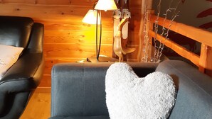 A cozy room with a blue sofa, a black leather chair, a wooden wall, a cow painting, a lamp, and a decorative deer head.