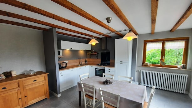 A modern kitchen with white cabinets, a dining table, and a window with a view of greenery.