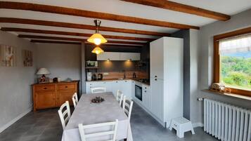 A modern kitchen with white cabinets, a dining table with chairs, and a window with a view of greenery.