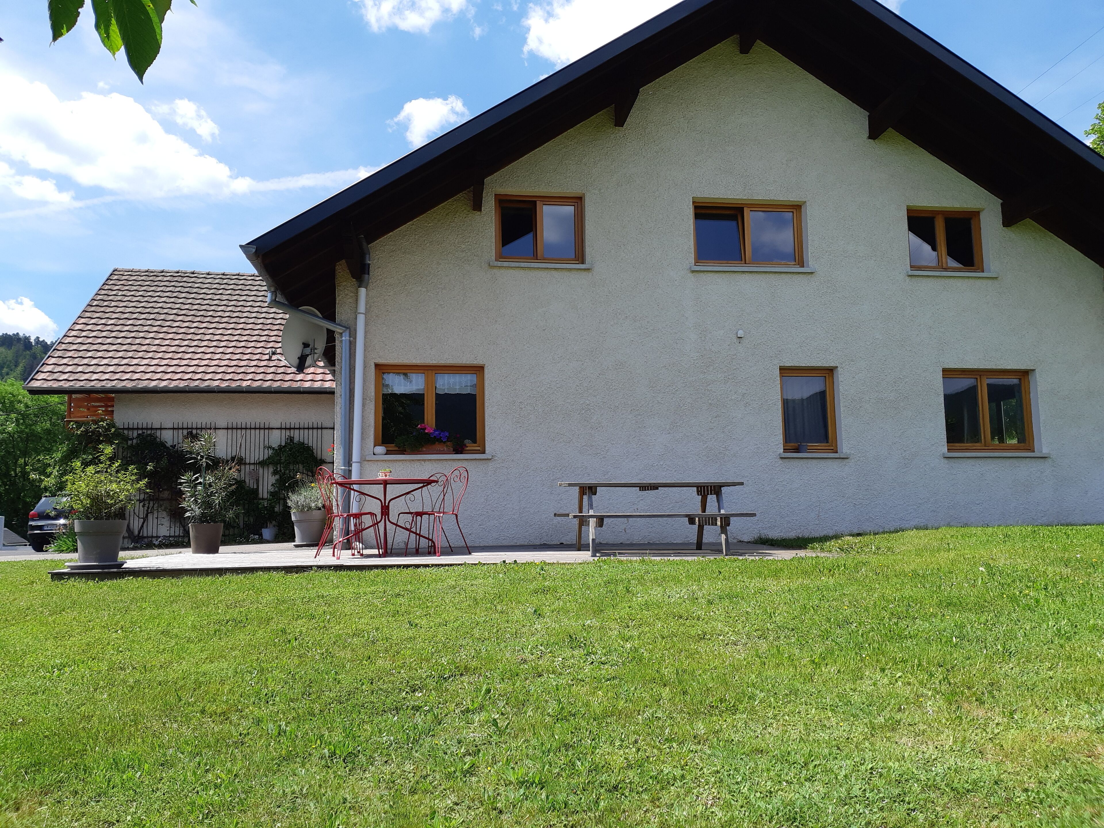A two-story house with a sloped roof, multiple windows, and a small patio with a table and chairs.