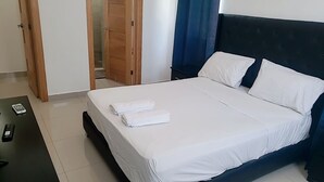 A neatly made bed with white linens and pillows, a bedside table with a phone, and a door leading to a bathroom. - Hotel boca del mar Bocachica playa   (Boca Chica)