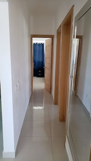 A hallway with a tiled floor, wooden doors, and a blue curtain visible in the distance. - Hotel boca del mar Bocachica playa (Boca Chica)