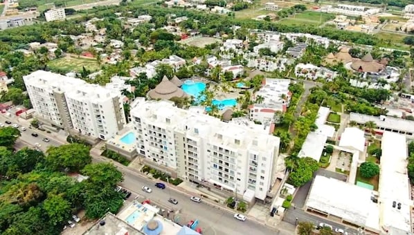 A high-rise residential building with multiple balconies, a swimming pool, and a well-maintained garden area. - Hotel boca del mar Bocachica playa (Boca Chica)