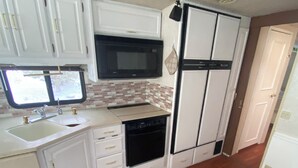 Une cuisine de taille réduite, avec des meubles blancs, un four à micro-ondes, un lave-vaisselle et un réfrigérateur.