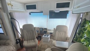 Un intérieur de camping-car compact comprenant deux fauteuils beiges, une petite table et un coin cuisine.