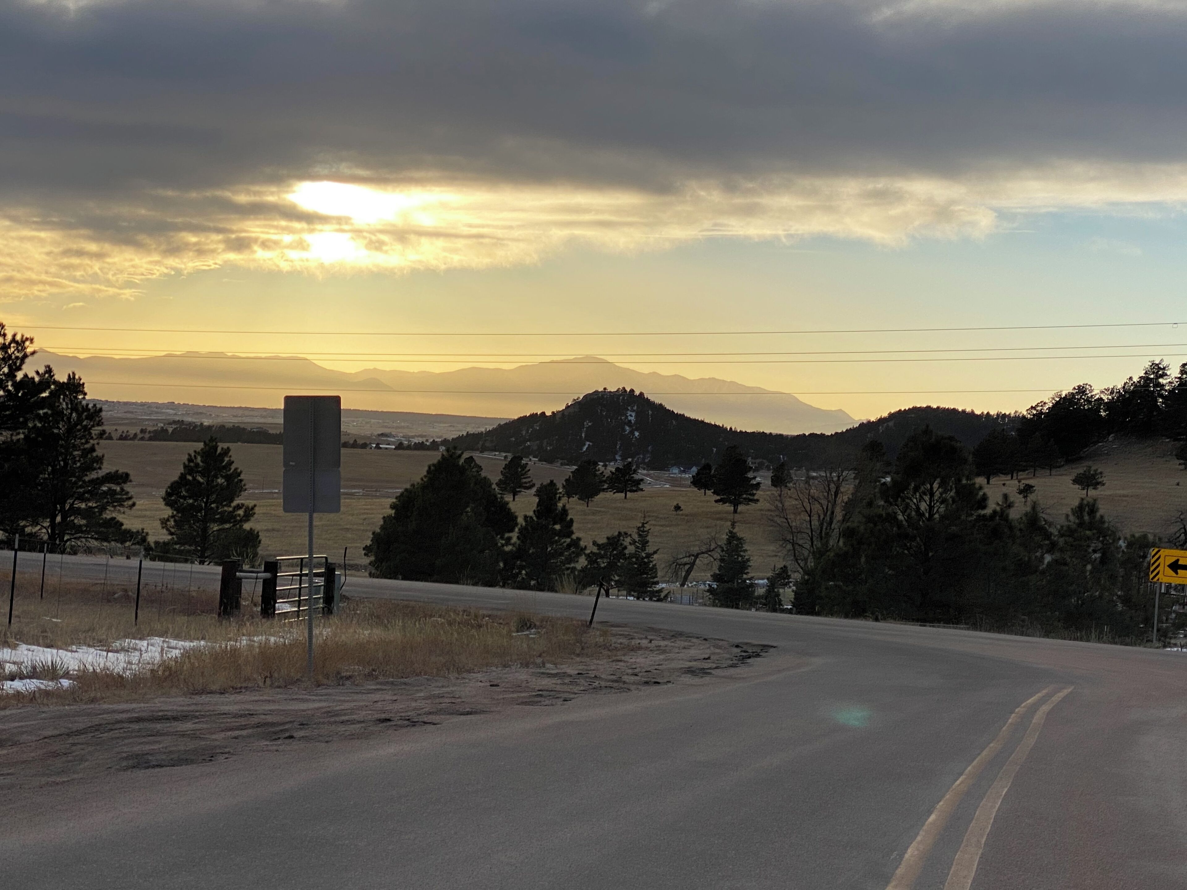 A road curving through a rural landscape with mountains in the distance and a sunset in the sky.