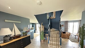 Amplia sala de estar con una escalera, un comedor y una cocina al fondo.