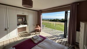 Un dormitorio con una cama, una tocador con espejo y vistas a un área verde a través de una puerta corrediza de vidrio.