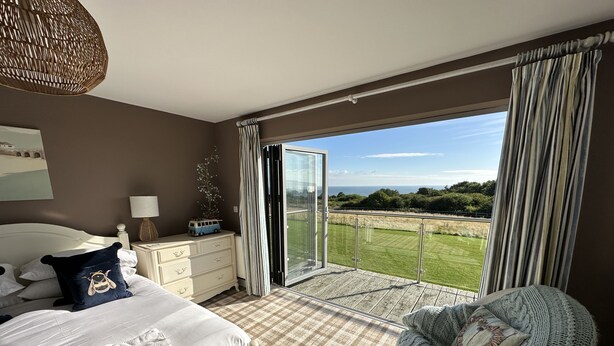 Un dormitorio con cama, mesita de noche, cómoda, una silla y un balcón con vista al paisaje.