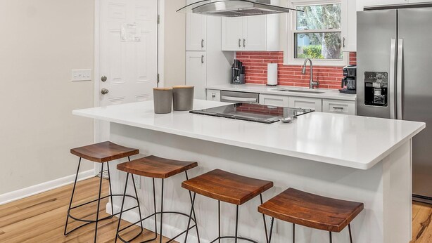 A modern kitchen with a large island, bar stools, stainless steel appliances, and a view of greenery outside.