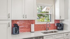 A modern kitchen with white cabinets, a red brick backsplash, stainless steel appliances, and a window with a view of greenery outside.