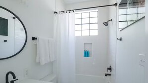 Un baño moderno con lavamanos, espejo y zona de ducha blanca.