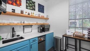 Una cocina moderna con armarios azules, un lavamanos de acero inoxidable, un microondas y un tostador. Hay estantes de madera sobre la encimera con varios utensilios de cocina.