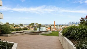 A rooftop terrace with a view of a city skyline, including a prominent chimney.