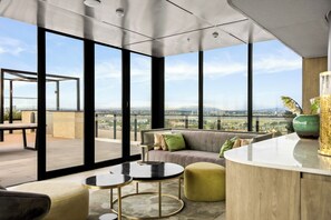 A modern living room with large windows, a sofa, a coffee table, and a small round table. - Contemporary Comfort (Footscray)