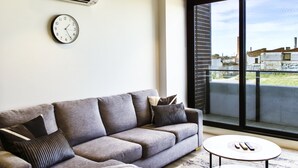 A modern living room with a grey sofa, a round coffee table, and a large window with a view of buildings.