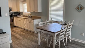 A kitchen with white cabinets, a wooden dining table, and a window with blinds. - 3 blocks from Taylors Creek, 1 mile from Beaufort waterfront and boat ramp (Beaufort)