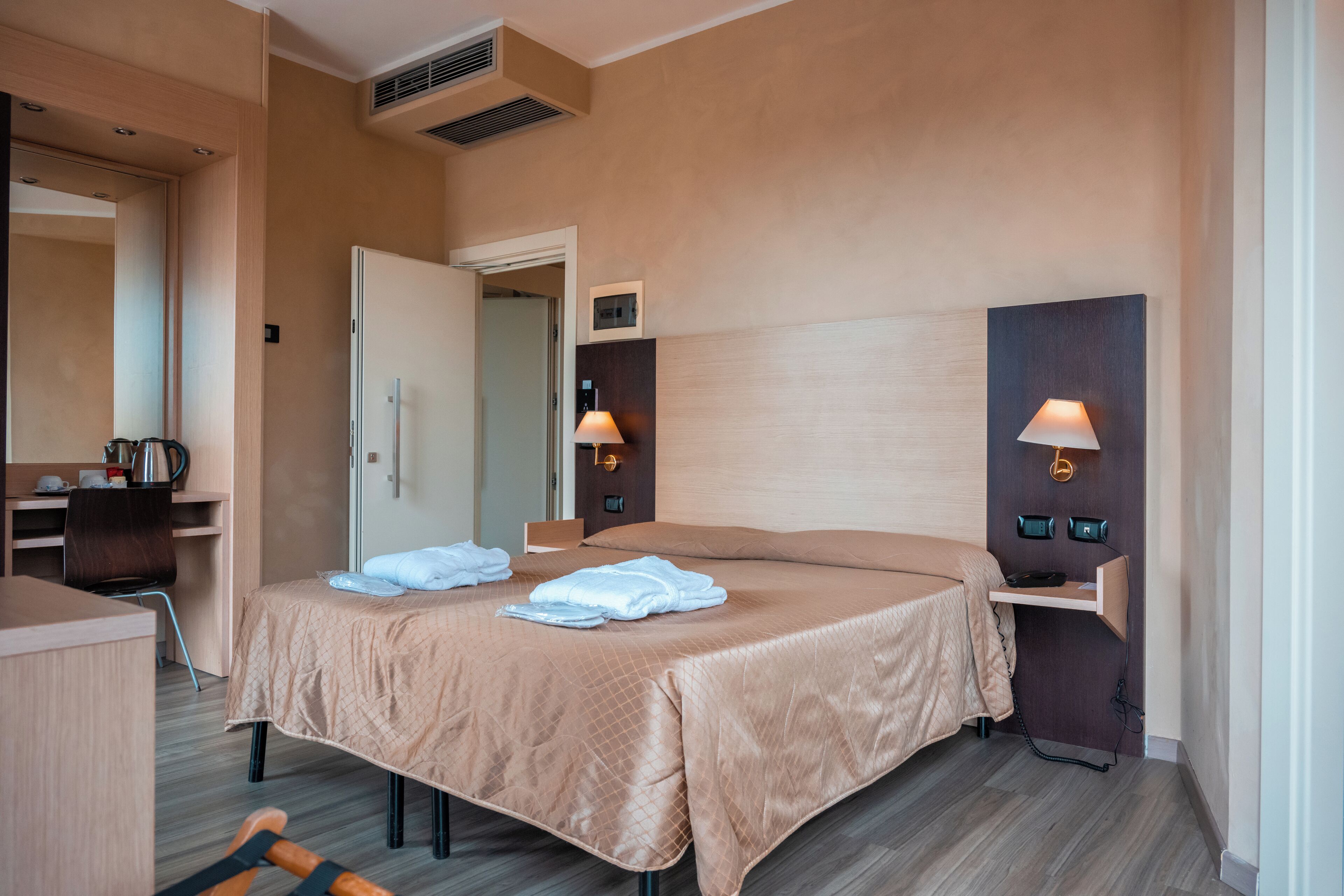 Quarto de hotel com cama, mesa de cabeceira, abajur e escrivaninha com cadeira.