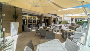 Un espace extérieur aménagé en terrasse, avec des meubles en osier, de grands parasols et un mur en pierre.
