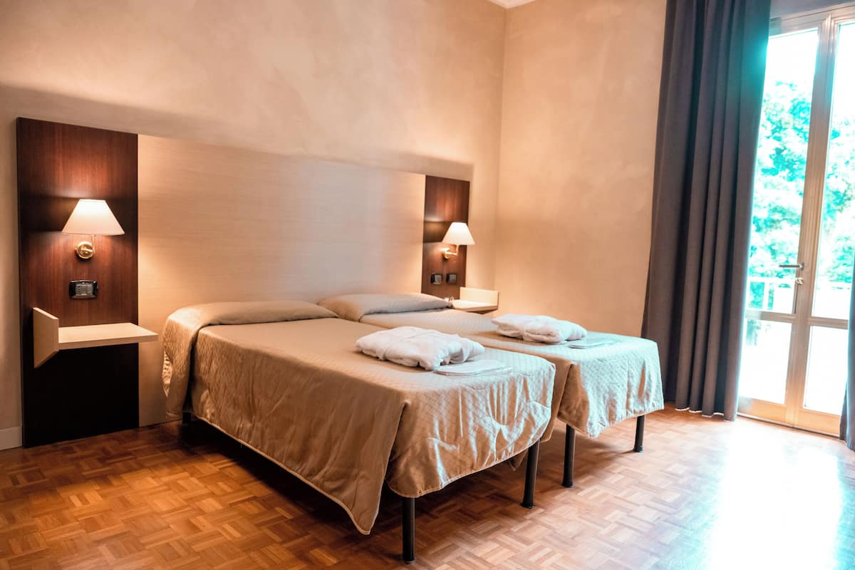 Quarto de hotel com duas camas, piso de madeira e uma janela grande com cortinas.
