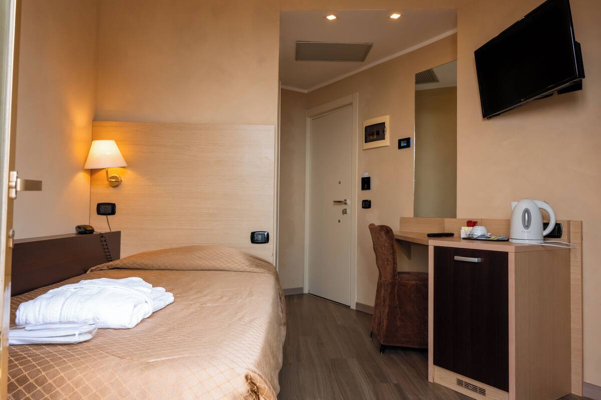 Quarto de hotel com uma cama, uma mesa com cadeira, televisão e cafeteira.