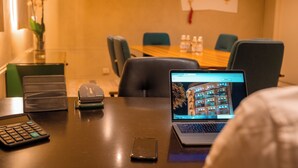 Une chambre d’hôtel avec un ordinateur portable sur un bureau, une calculatrice, un téléphone portable et un vase rempli de fleurs.
