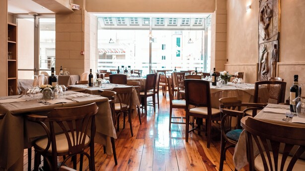 Un restaurant doté d’un plancher en bois, de tables dressées avec des verres à vin, et offrant une vue sur les bâtiments à travers de grandes fenêtres.