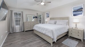 Ein Schlafzimmer mit einem Bett, Nachttischen, einer Kommode, einem Deckenventilator und einem Fenster mit Vorhängen.