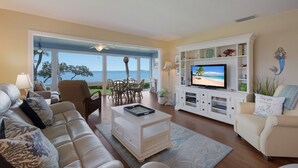 Un soggiorno con un'ampia TV, posti a sedere confortevoli, zona pranzo e vista mare.