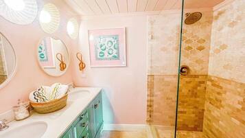 Un baño con mampara de vidrio, un lavabo con una cesta de toallas y detalles decorativos en la pared.