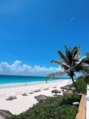 A beach with white sand, clear blue water, and a few people. There are umbrellas and lounge chairs along the shore. - Fig Tree Harbour Island 3 Bedroom Home (Dunmore Town)