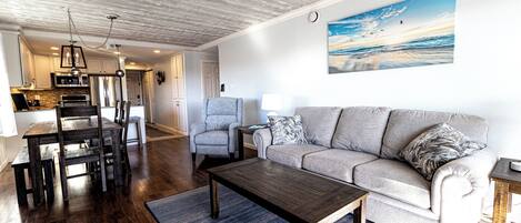 A modern living room with a wooden coffee table, a grey sofa, and a dining area with a wooden table and chairs.